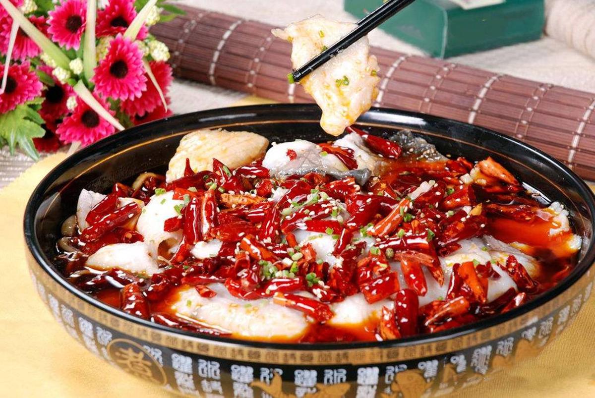 Sichuan Boiled Fish — the bowl on a restaurant table with chopsticks reaching in, steam visible, rice bowl on the side