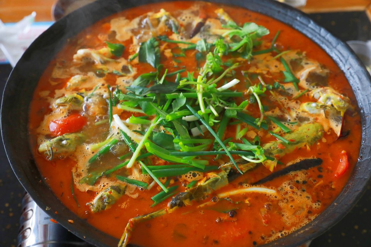 Close-up of the pot at a rolling bubble — chunked fish, tomato, scallion and chili swimming in the red-orange sour broth