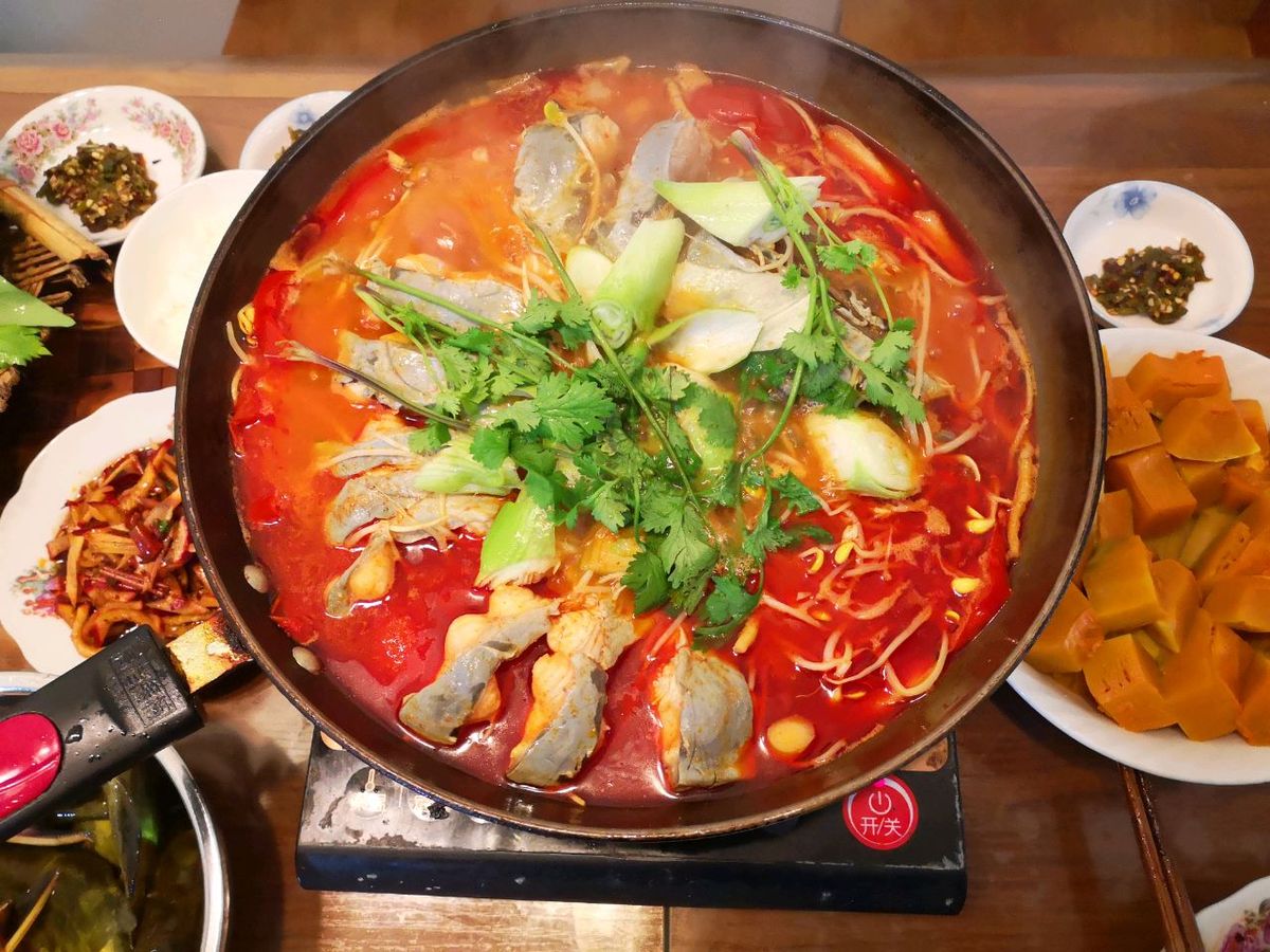 Sour soup fish at the table — the pot on a tabletop burner with rice, condiment bowls and side dishes spread around it