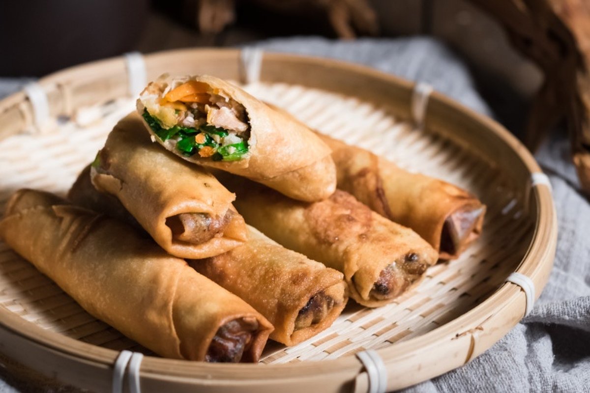 Spring roll close-up — broken in half, cross-section revealing shredded pork, cabbage, and mushroom filling, steam rising, flaky wrapper layers visible