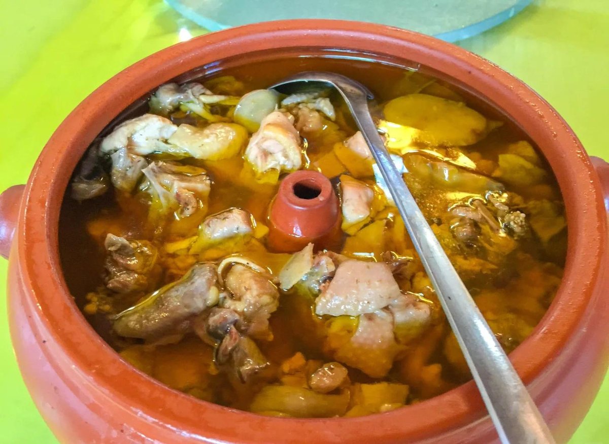 Steam-Pot Chicken — a whole chicken in a shallow pool of golden broth inside a traditional Yunnan clay steam pot with its central chimney