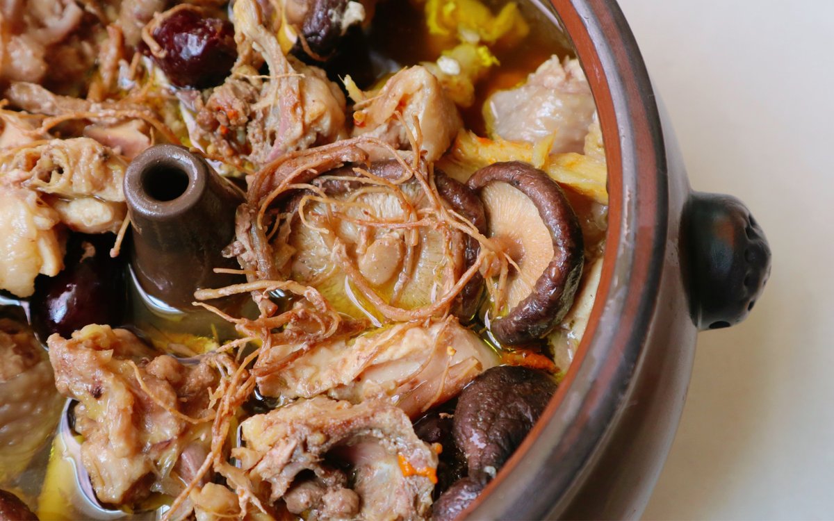 Steam-Pot Chicken close-up — chicken, shiitake, ginseng root and red dates in the clear amber broth around the chimney