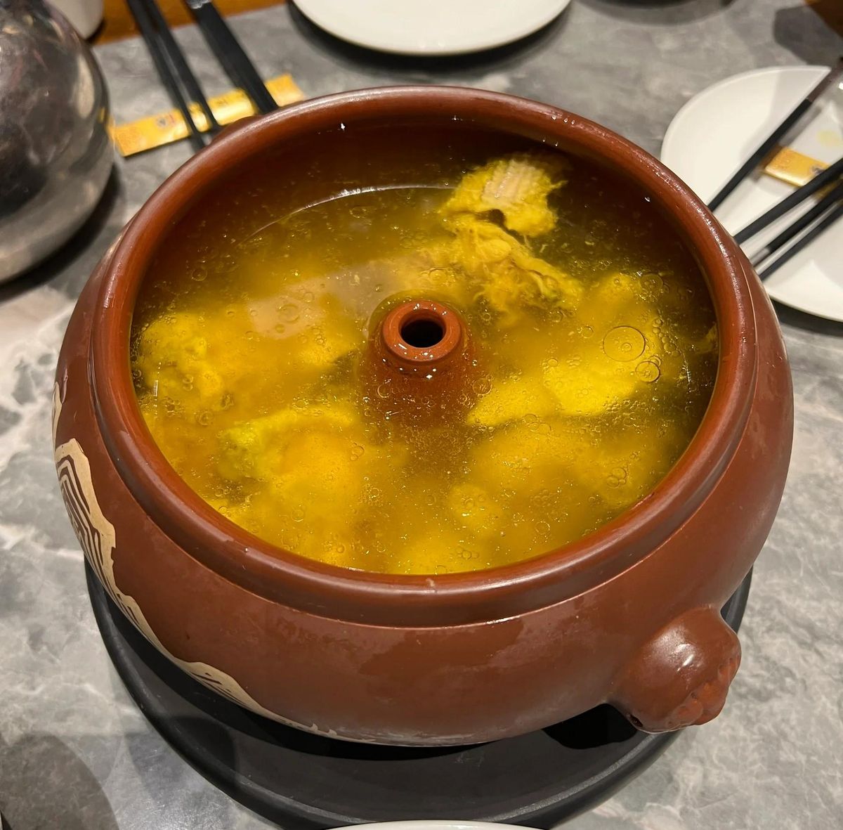 Steam-Pot Chicken served at a restaurant table — the clay pot with chopsticks and plates, the way it arrives in Yunnan