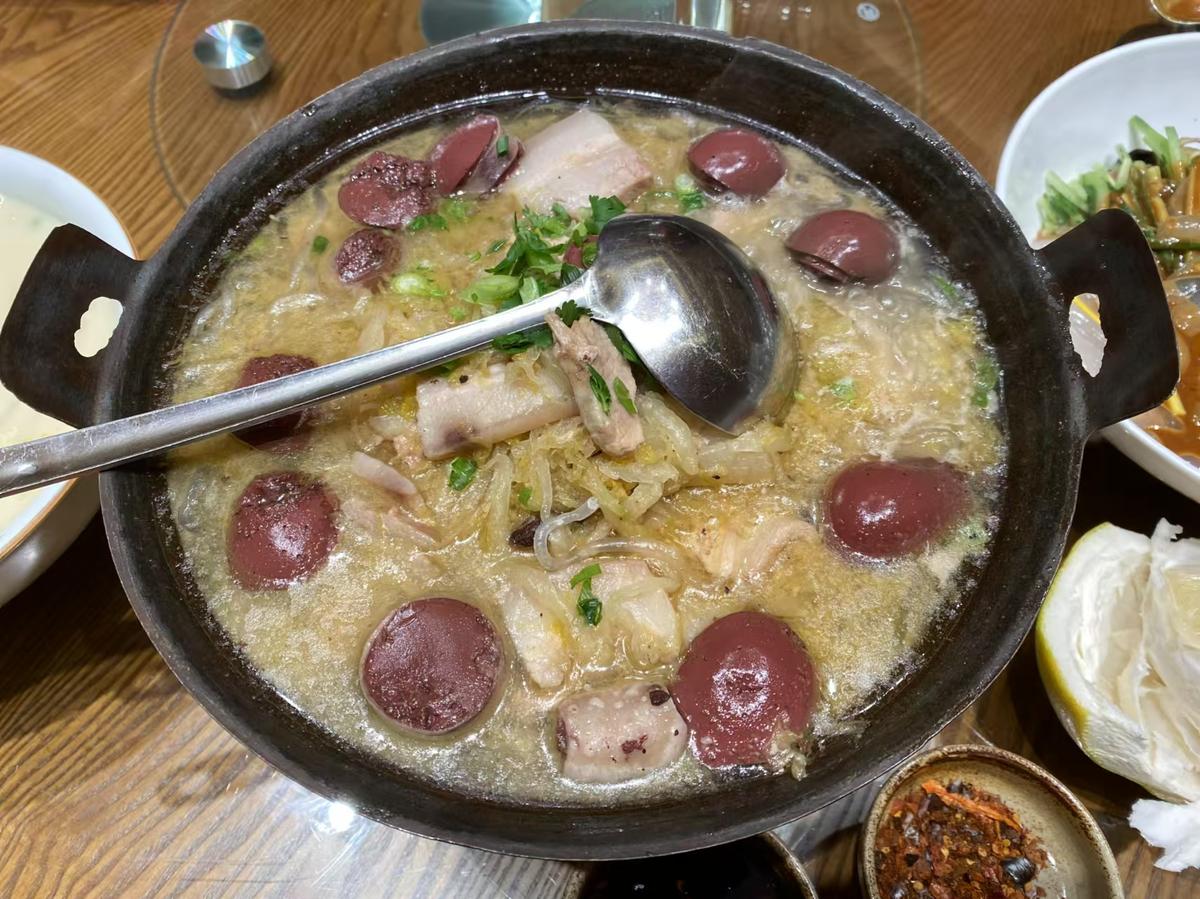 Suan Cai Bai Rou — a Dongbei pot of fermented napa cabbage with sliced pork belly, blood sausage and glass noodles, a ladle resting across the rim