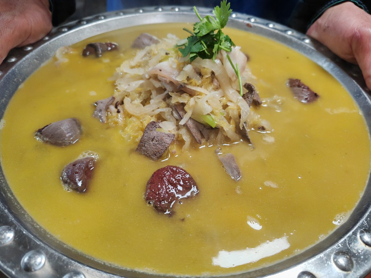 A wide pan of the Dongbei kill-the-pig stew — suan cai with white-cut pork belly and blood sausage — carried to the table