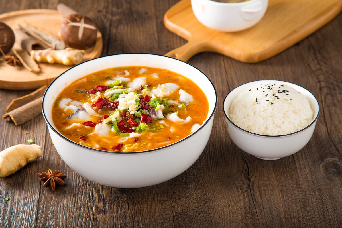 Suan Cai Yu served in a large bowl over a casual table setting — chopsticks reaching for a fillet