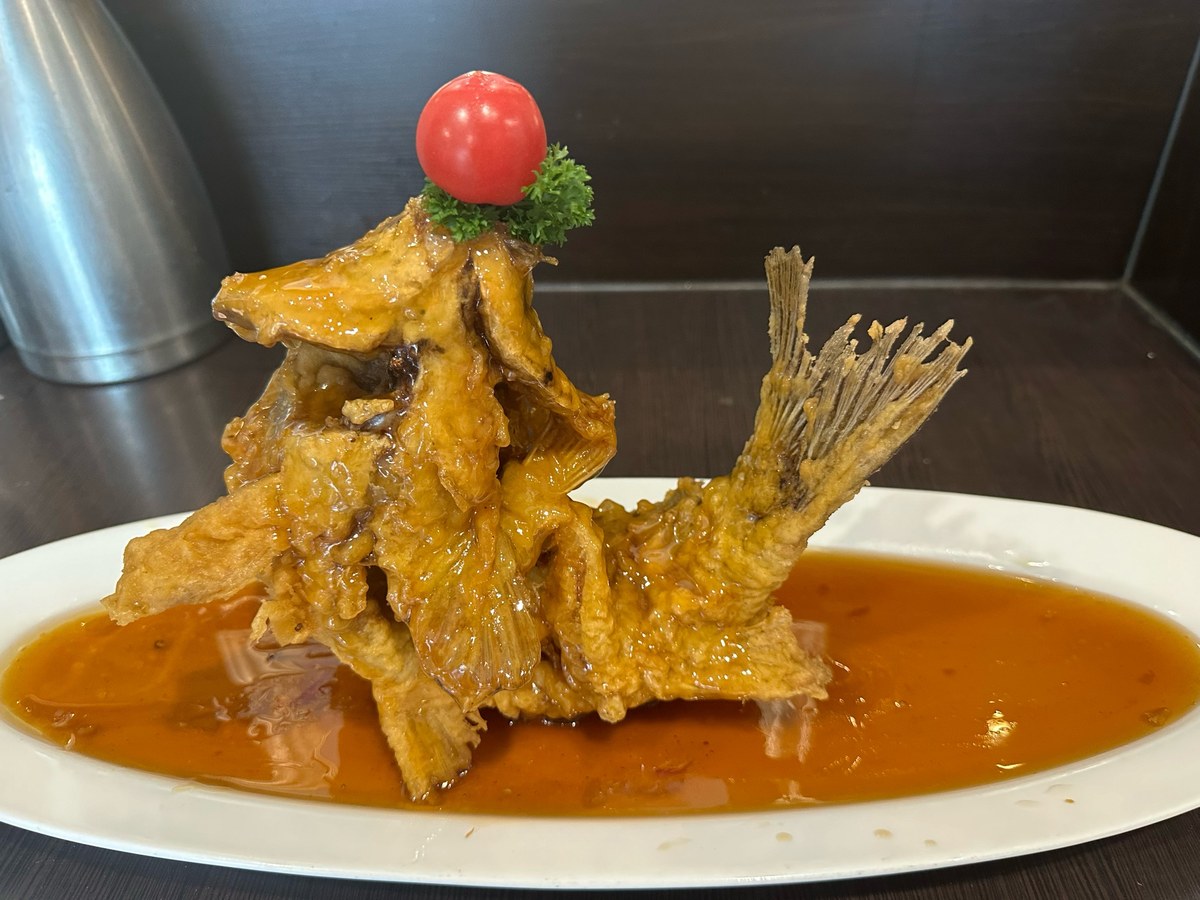 Sweet-and-sour carp close-up — deep crosshatch scores fanned open like a pinecone beneath translucent amber sauce