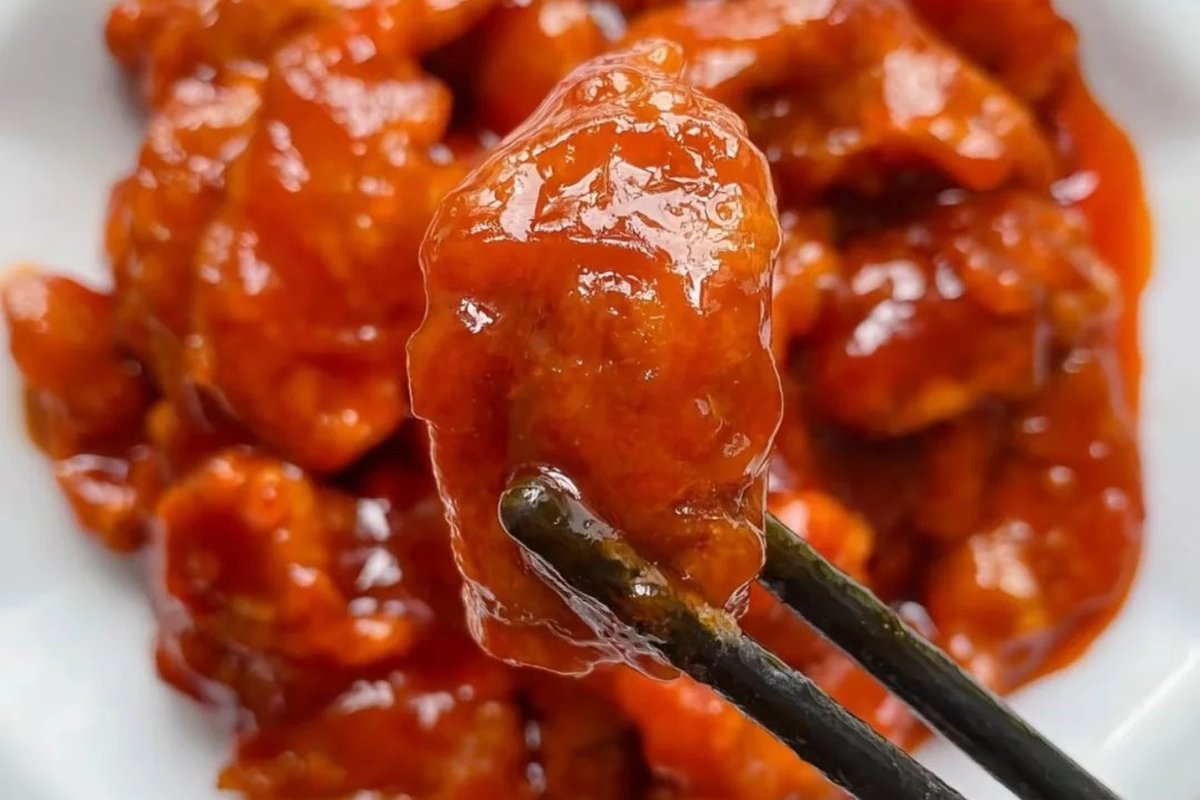 Sweet and Sour Pork — the dish served over white rice with chopsticks reaching in, sauce glistening