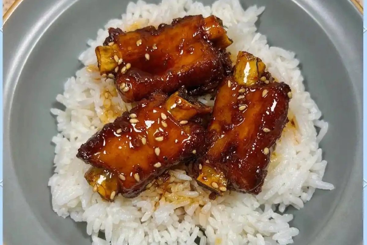 Tang Cu Pai Gu over steamed rice — dark glazed ribs resting on a bed of white rice, chopsticks lifting a glistening piece