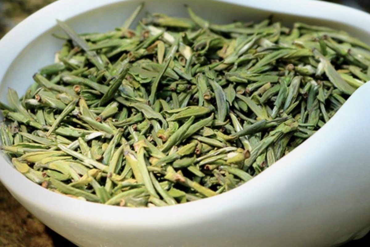 Dry, flat green tea leaves piled in a shallow white porcelain tea presentation dish, a 茶荷, lit from the side