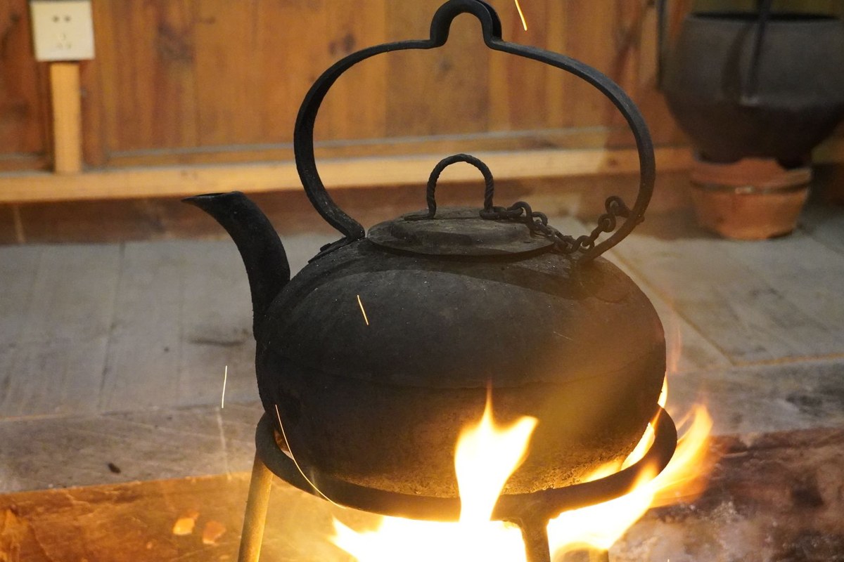 A black cast-iron kettle hanging over an open fire, flames licking the base