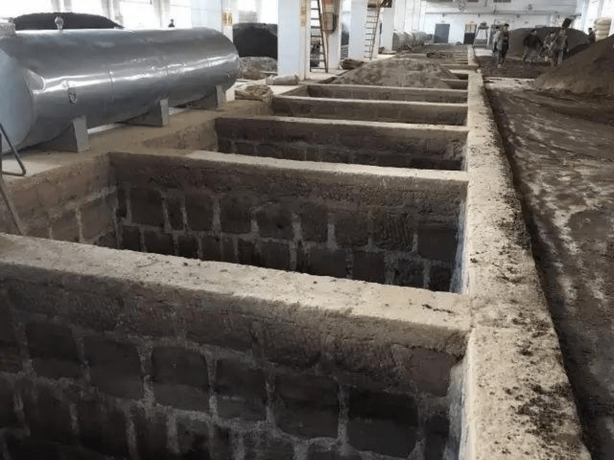 A row of open fermentation pits sunk into the floor of a Luzhou distillery hall, brick-lined and waiting for grain