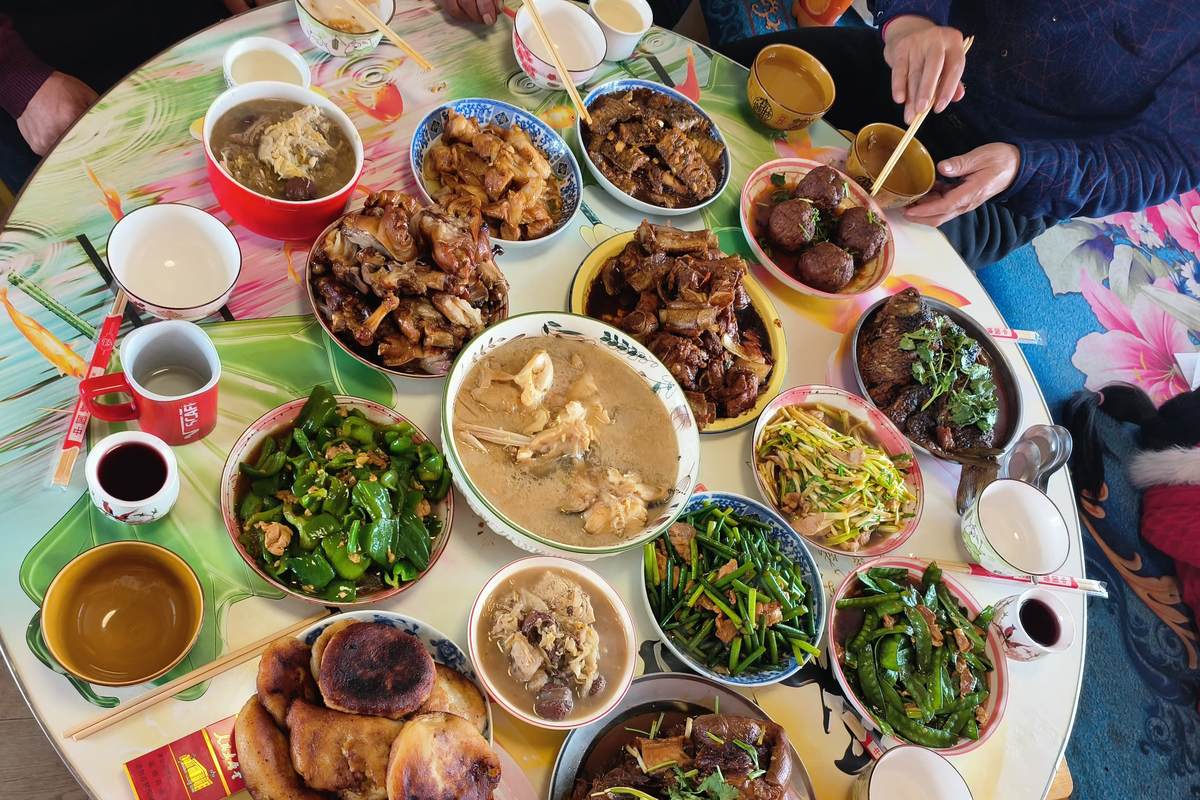 An overhead view of a round family table crowded with dishes, bowls, chopsticks and small cups