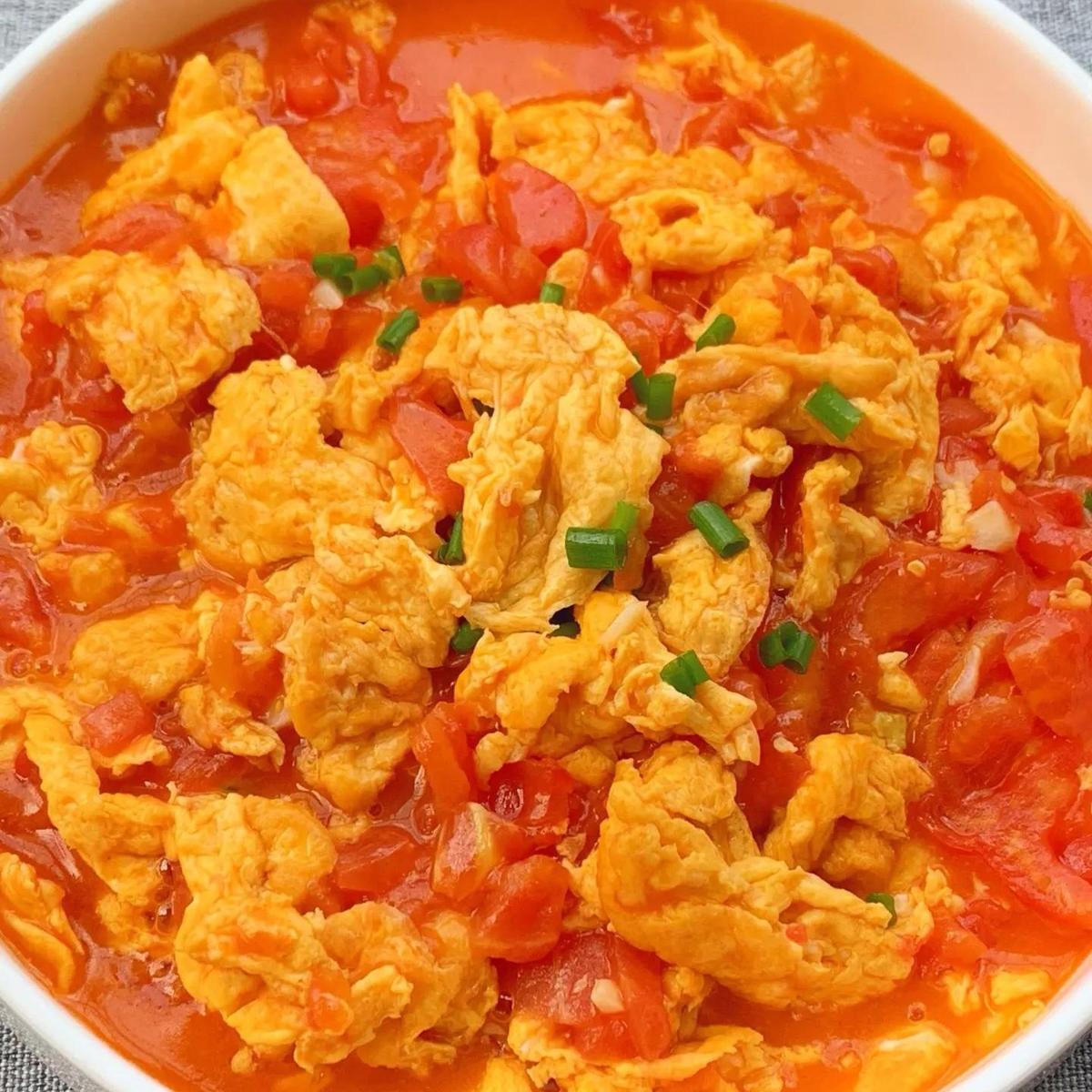 Tomato and Egg Stir-fry — glossy scrambled eggs and jammy tomato wedges in a glossy sauce, served family-style in a ceramic bowl on a wooden table