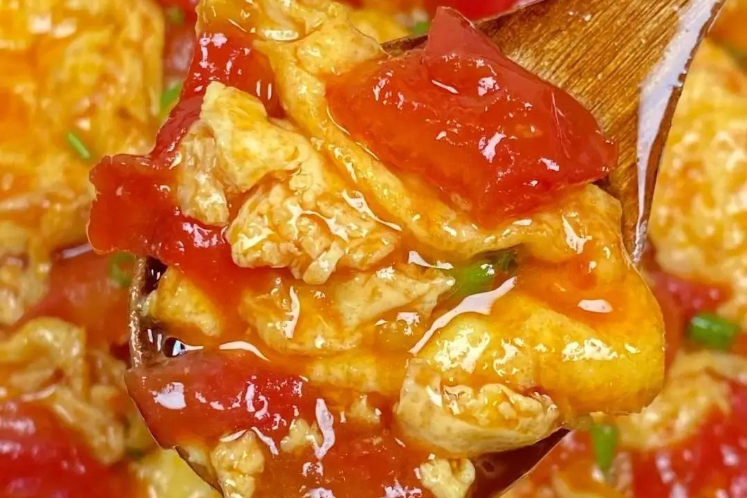 Close-up of chopsticks lifting a fold of silky egg draped over a tomato wedge — sauce glistening, steam rising in soft wisps