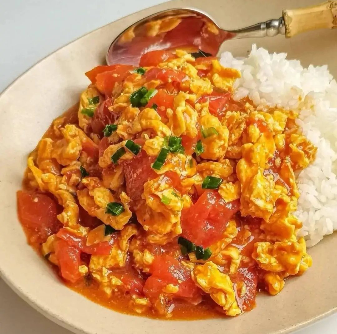 Tomato and Egg Stir-fry served in a blue-and-white porcelain bowl beside a bowl of steamed jasmine rice — chopsticks resting on a ceramic rest