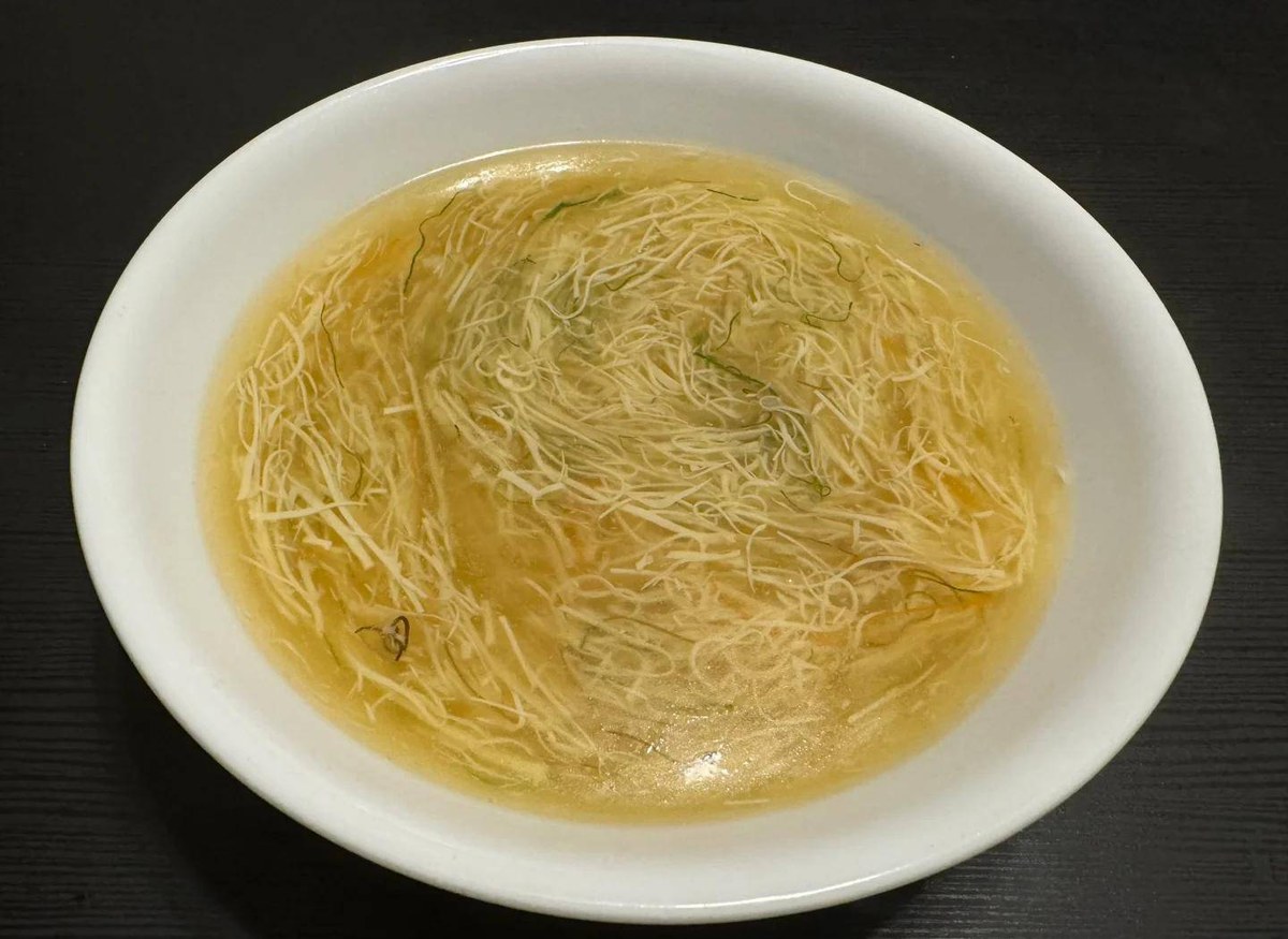 Wensi Tofu — close-up of the tofu threads suspended in the broth of a white porcelain bowl on a dark table