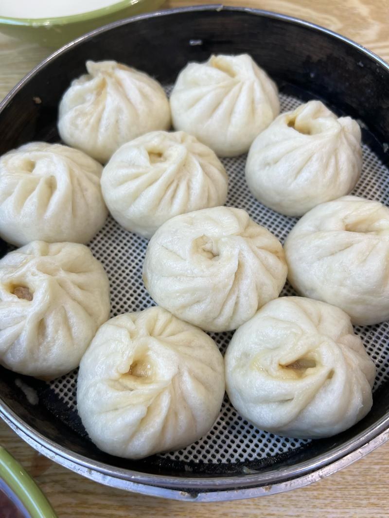 Xiao Long Bao in a bamboo steamer — translucent skins shimmering with broth sealed inside, steam rising