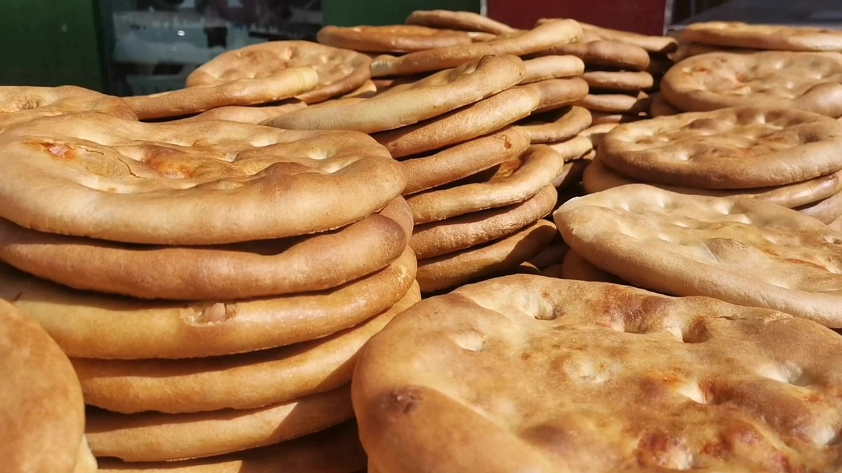 Xinjiang naan — a heap of freshly baked rounds with puffed rims and blistered centres, stacked at a street stall