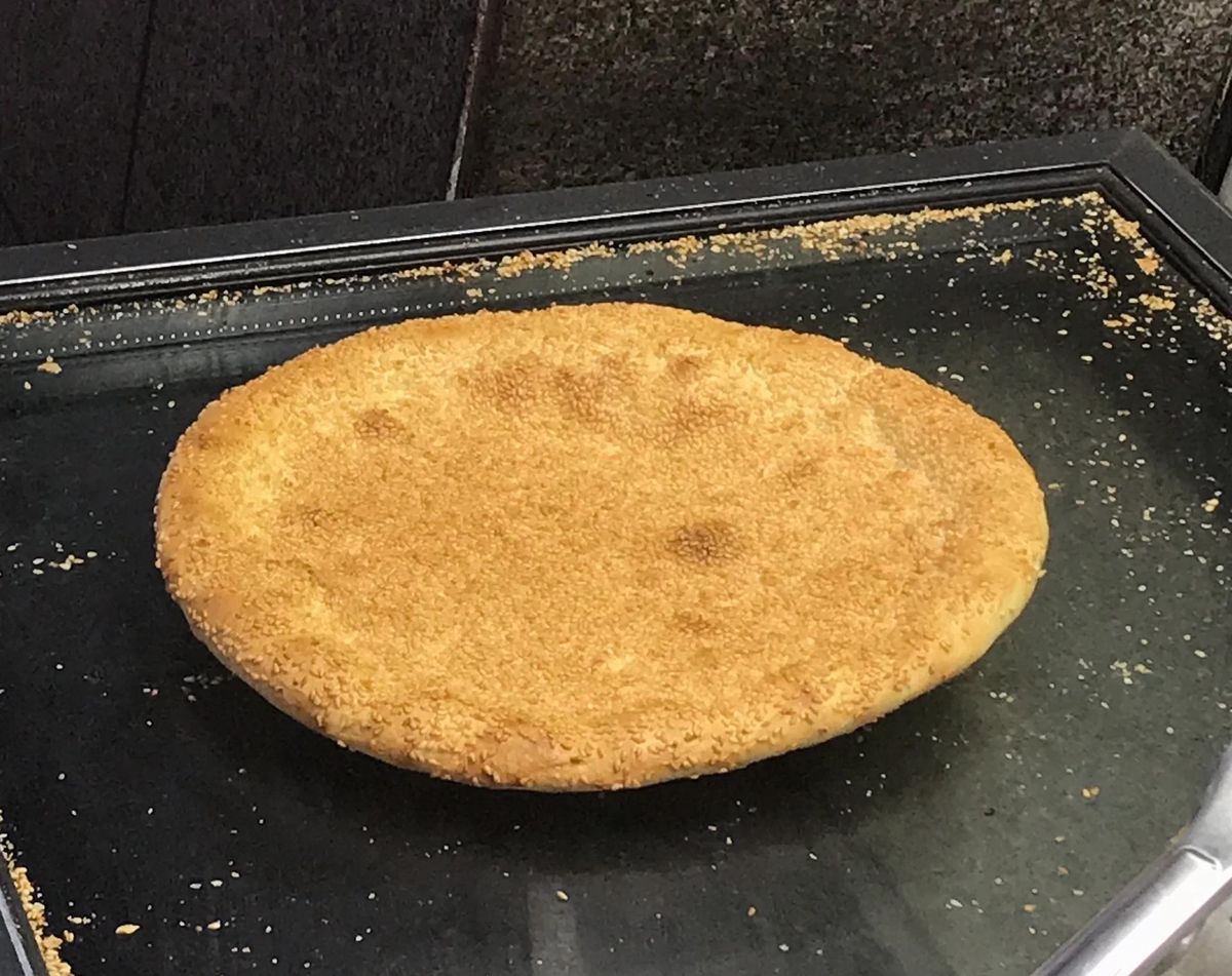 A single sesame naan — stamped dimpled centre, blistered middle band and raised outer ring, seeds scattered around
