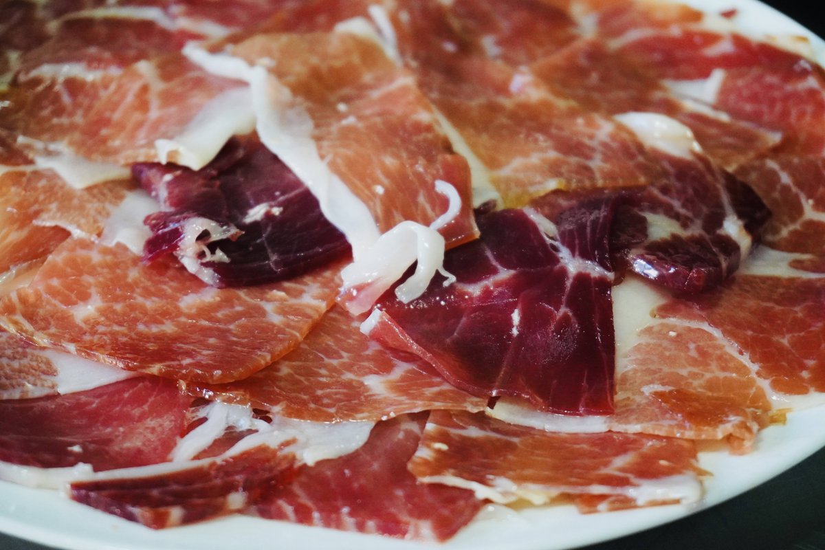 Xuanwei ham — thin raw slices of dark-red cured ham, marbled white, fanned on a white plate