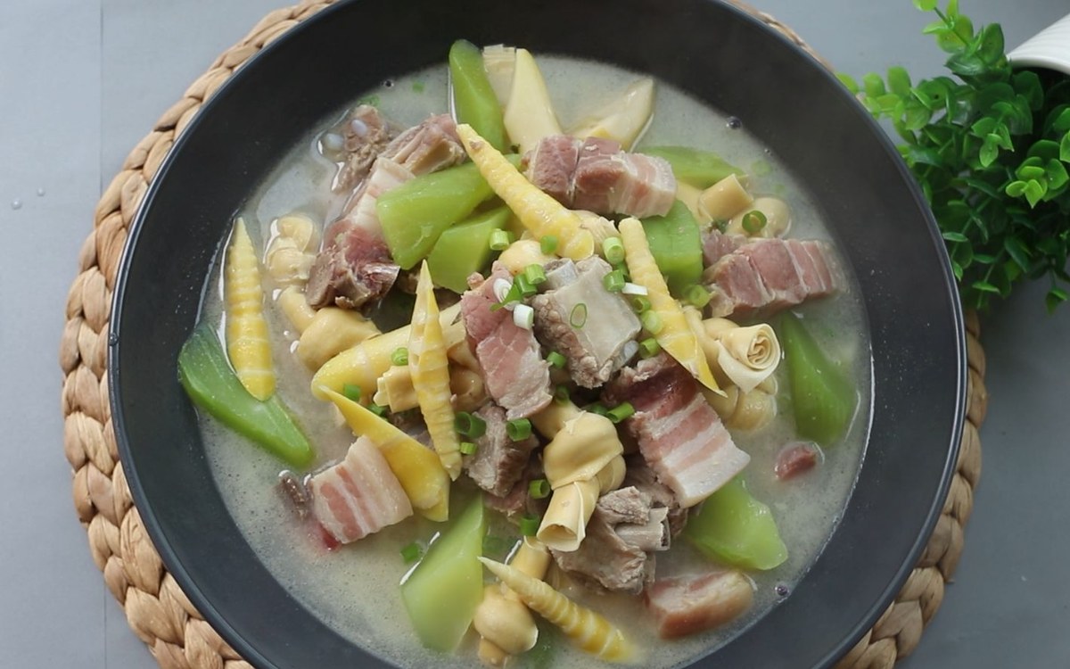 Yan Du Xian — an overhead bowl of pale pork and bamboo shoot broth with scallions, on a woven trivet