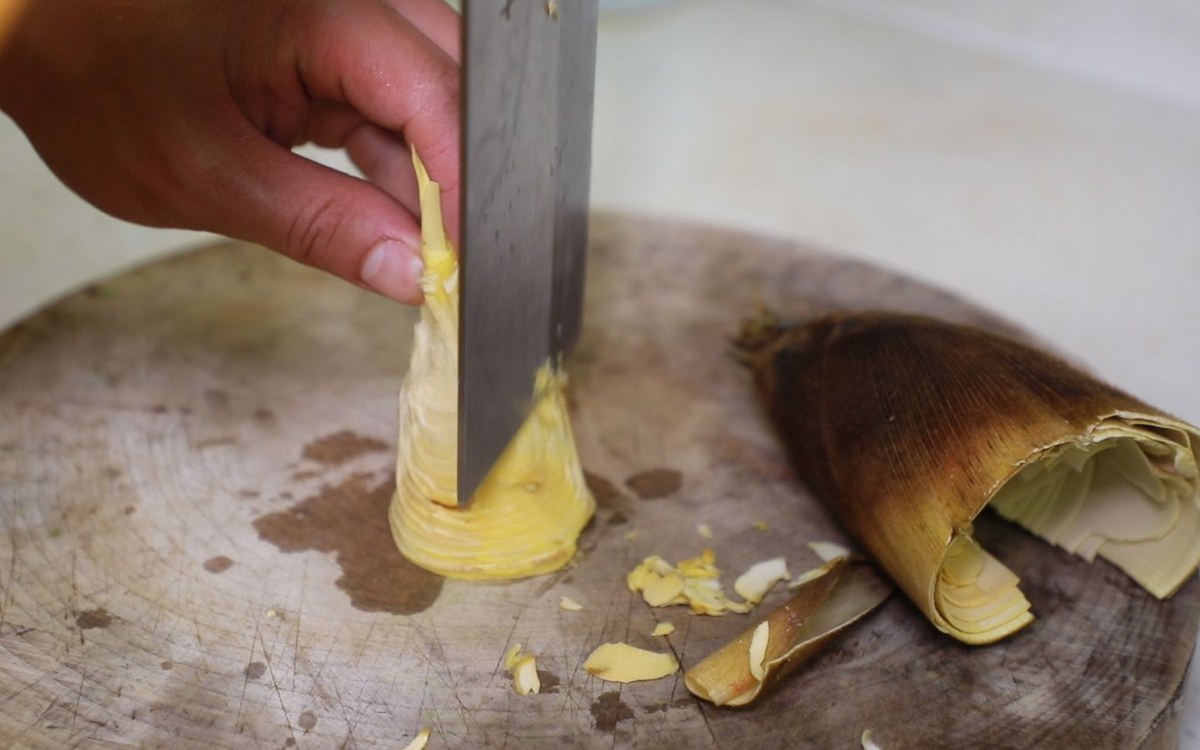 Spring bamboo shoots — a hand splitting a fresh shoot with a cleaver on a worn wooden board