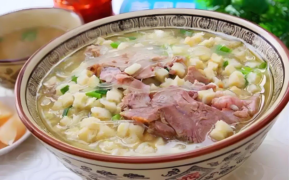 Yangrou Paomo — close-up of hand-torn bread pieces with ragged edges soaking in golden lamb broth