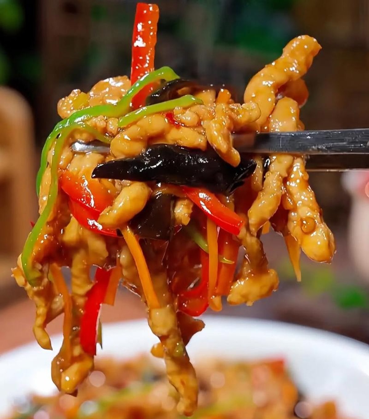 Close-up: strands of velvety pork coated in the signature yu xiang sauce — glossy, amber, studded with scarlet chili flecks and pale slivers of garlic