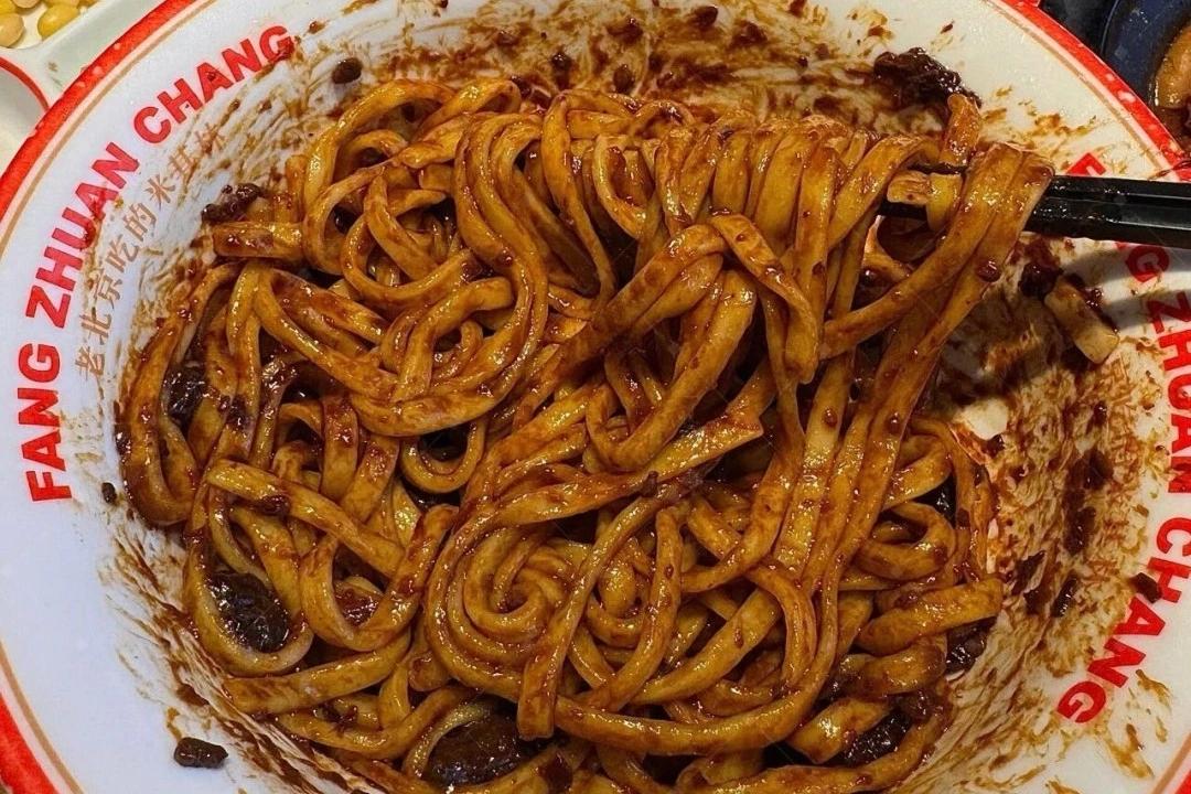 Zha Jiang Mian — closeup of dark fried sauce clinging to thick wheat noodles, diced pork belly visible in the sauce