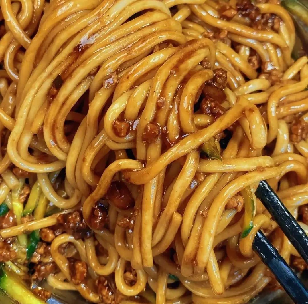 Zha Jiang Mian — the fully mixed bowl, every strand coated in dark sauce, ready to eat with chopsticks